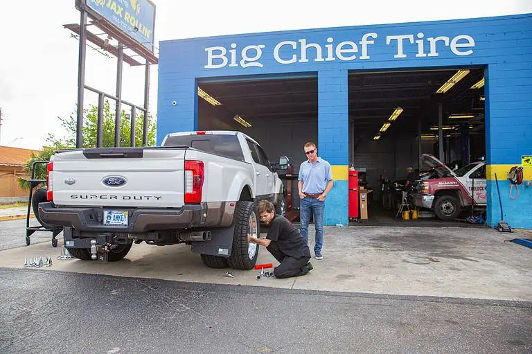 Exterior of BCT as man works on tire of vehicle while customer watches