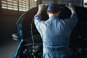 mechanic with back toward camera working on under hood of car